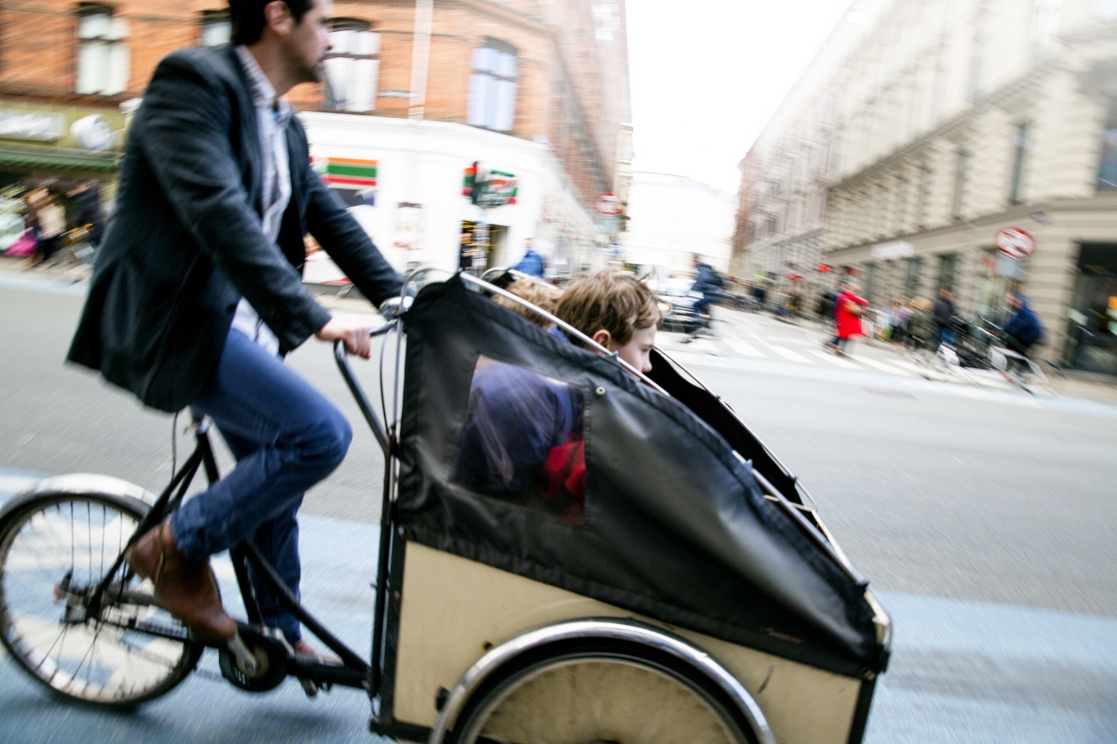 A parent riding a cargo bike through a city street with two children in the box
